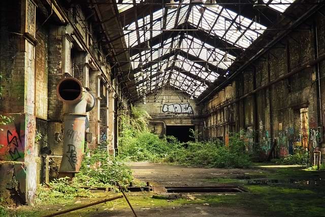 Photo of an abandonned factory, that is tagged and getting invaded by vegetation. This is a pretty vivid representation of some legacy code.